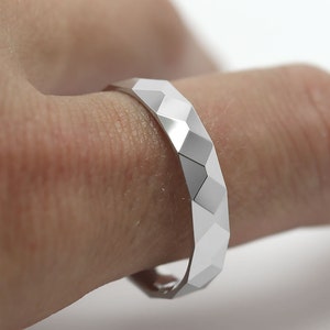 May include: A silver ring with a geometric, faceted design. The ring is worn on a finger.