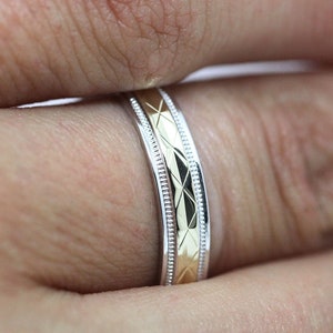 Pode incluir: Um close-up de uma alian&ccedil;a de dois tons com um design em ouro e prata. A alian&ccedil;a tem um padr&atilde;o texturizado e um acabamento polido.