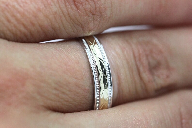 Pode incluir: Um close-up de uma alian&ccedil;a de dois tons com um design em ouro e prata. A alian&ccedil;a tem um padr&atilde;o texturizado e um acabamento polido.