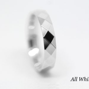 May include: A white gold ring with a geometric design. The ring has a diamond-shaped pattern with a black center.