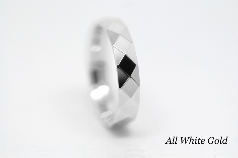 May include: A white gold ring with a geometric design. The ring has a diamond-shaped pattern with a black center.