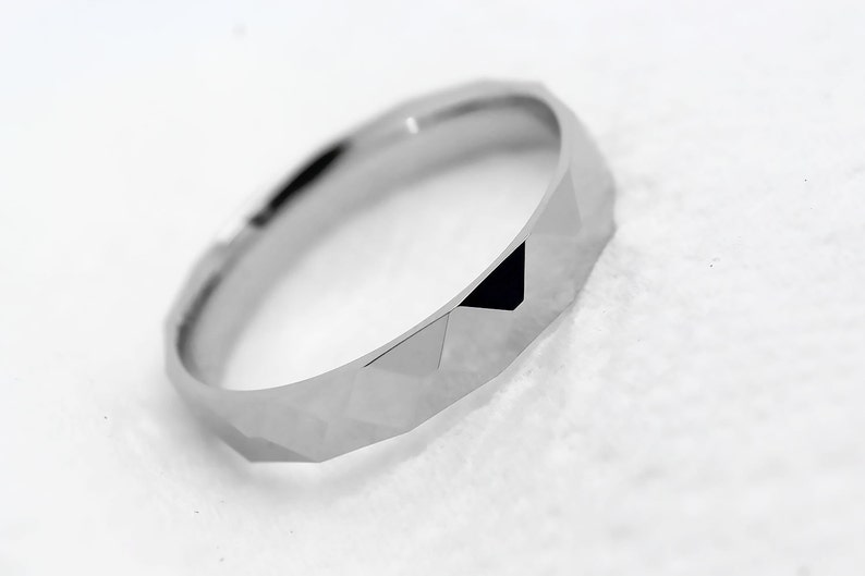 May include: A silver ring with a geometric, faceted design. The ring is made of a smooth, polished metal.