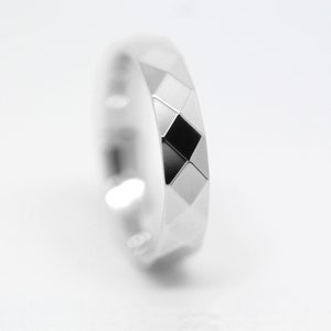 May include: A silver ring with a geometric design. The ring has a black diamond-shaped pattern in the center.