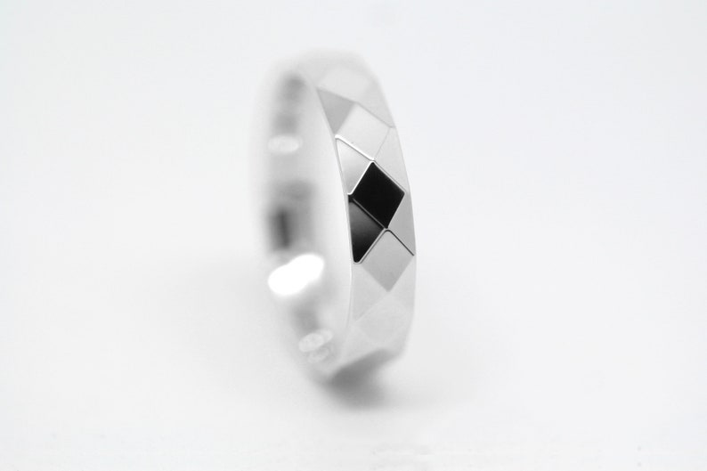 May include: A silver ring with a geometric design. The ring has a black diamond-shaped pattern in the center.