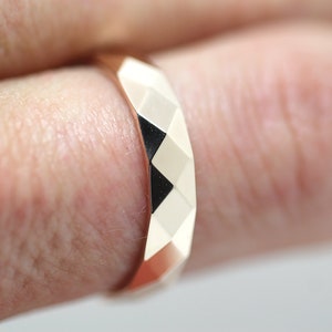 May include: A rose gold ring with a faceted design. The ring is worn on a finger.