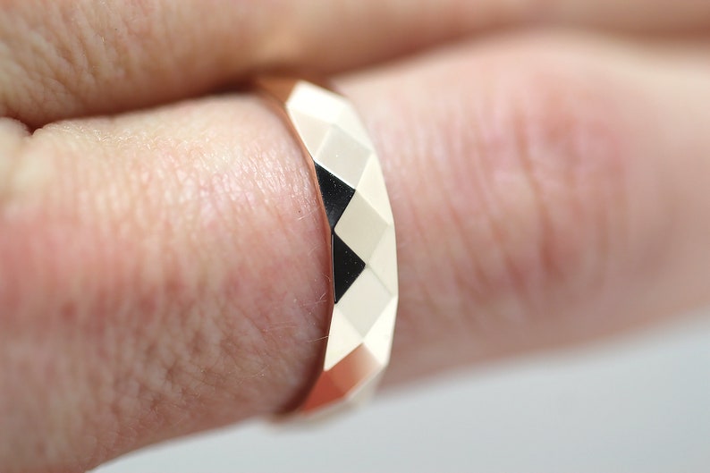 May include: A rose gold ring with a faceted design. The ring is worn on a finger.