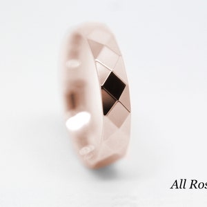 May include: A rose gold wedding band with a geometric design. The band is made of a smooth, polished metal and has a slightly rounded edge. The band is a simple and elegant design that would be perfect for a wedding or engagement ring.