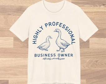 Op de afbeelding: Wit T-shirt met een blauwe afbeelding van twee eenden en de tekst "HIGHLY PROFESSIONAL BUSINESS OWNER definitely not a silly goose".