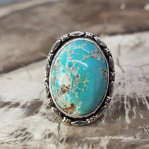 May include: A turquoise ring with a silver setting. The turquoise is a light blue colour with brown and white markings. The setting is oval shaped and has a decorative border.