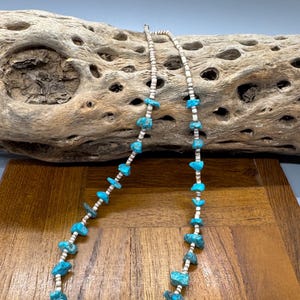 May include: A turquoise and white beaded necklace. The necklace features irregular, bright blue turquoise stones interspersed with small, white beads. The necklace is displayed on a wooden surface.