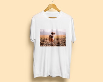 May include: White t-shirt with a photo of a brown and white dog standing in a field.