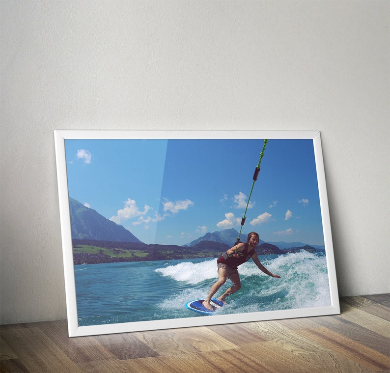 May include: A person wakeboarding on a lake with mountains in the background. The person is wearing a red shirt and blue shorts. The water is blue and the sky is clear.
