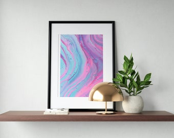 May include: A framed abstract print with pink, blue, and purple swirls hangs on a wall above a wooden shelf. A gold dome lamp and a potted plant with green leaves sit on the shelf.