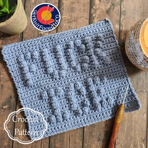 May include: A light blue crochet pattern with a textured, raised design. The pattern is rectangular and features a series of bobbles. The image also includes a crochet hook and a logo that says "Get Knit Faced Inco" and "Crochet Pattern".
