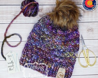 May include: A purple and brown knitted hat with a faux fur pom pom. The hat is on a wooden surface with a ball of yarn, a pair of scissors, and a tag that says "Yes I really made this!" and a knitting pattern.