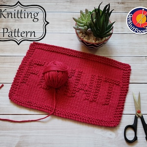 May include: Knitting pattern for a red dishcloth with the word "Knit" in raised stitches. The dishcloth is on a wooden surface with a ball of red yarn and a pair of scissors.