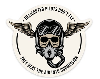 May include: A black and white sticker with a skull wearing a pilot's helmet and goggles. The skull has wings and the text "Helicopter Pilots Don't Fly. They Beat The Air Into Submission."