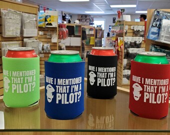 May include: Four different colored can coolers with the text "Have I mentioned that I'm a pilot?" and a cartoon pilot image. The can coolers are green, blue, black, and red.