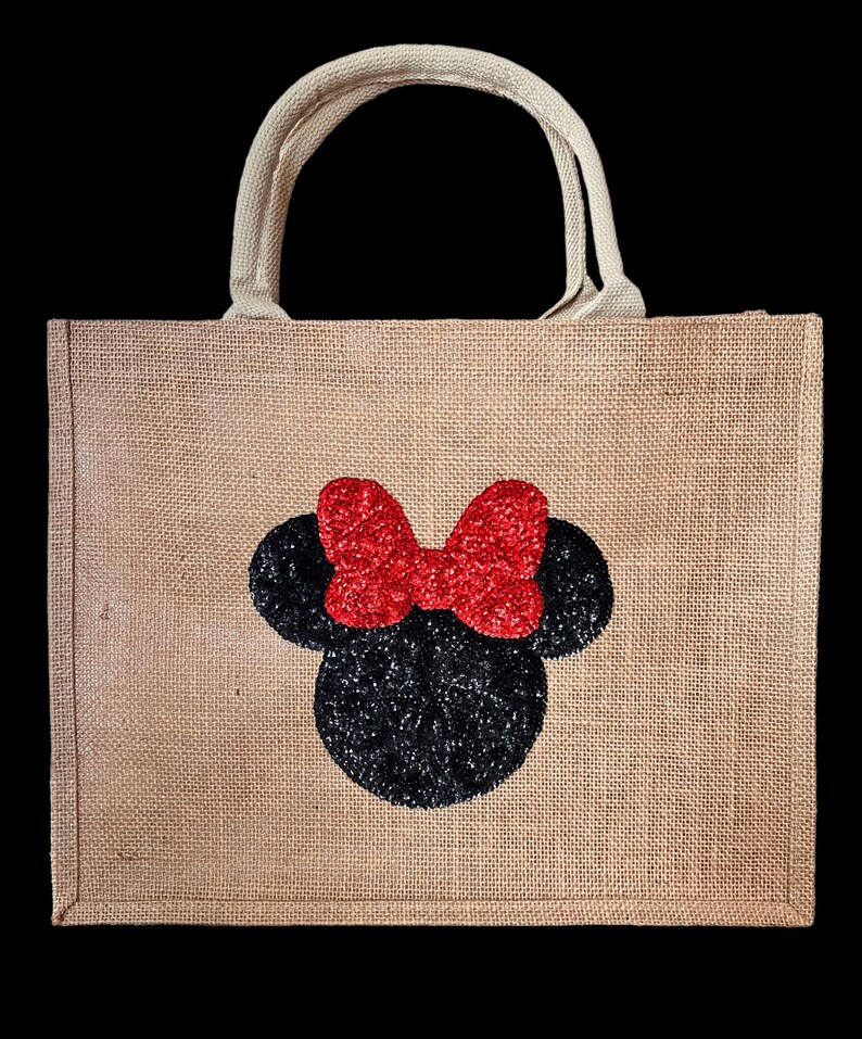 Op de afbeelding: Een beige jute draagtas met een zwart glitter muizenkopontwerp en een rode glitter strik. De tas heeft een bijpassende beige handgreep en is geschikt voor het dragen van diverse items.
