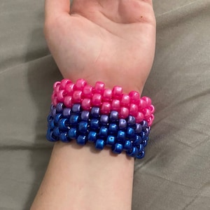 May include: A multi-colored beaded bracelet with pink, purple, and blue beads. The bracelet is made of small, square-shaped beads.
