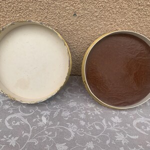 May include: Two round, lidded boxes. One box is white with a floral pattern and the other box is brown.