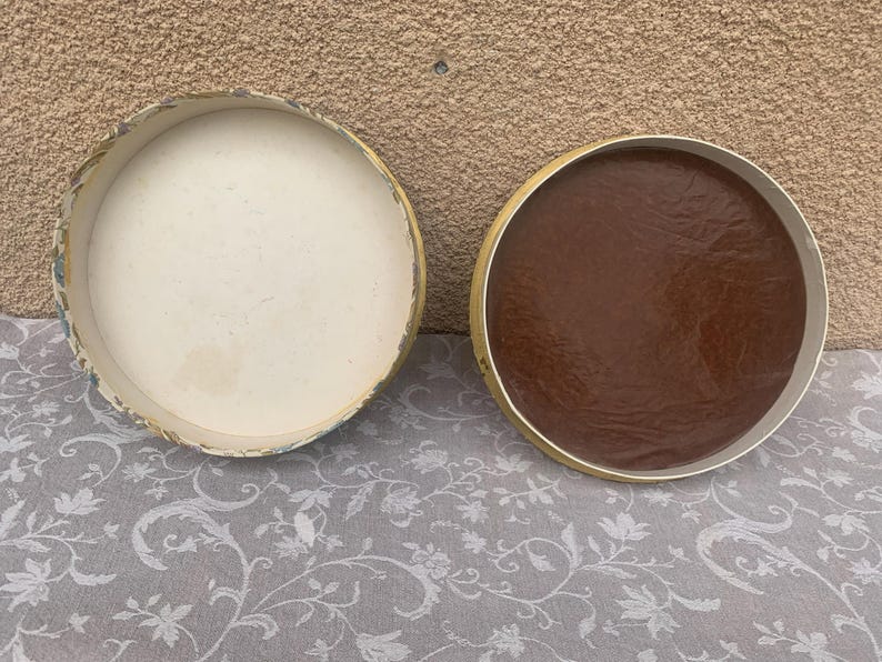 May include: Two round, lidded boxes. One box is white with a floral pattern and the other box is brown.