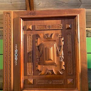 Op de afbeelding: Een houten deur met ingewikkelde houtsnijwerk. De deur is gemaakt van donker hout en heeft een rechthoekige vorm. De houtsnijwerk is in een bloemmotief en is zeer gedetailleerd.