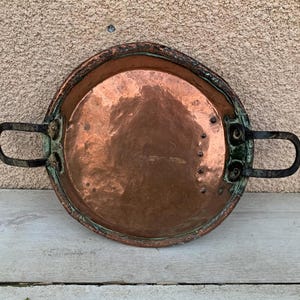 May include: A vintage copper pan with two black iron handles. The pan has a worn, rustic look and is perfect for adding a touch of farmhouse charm to your kitchen.