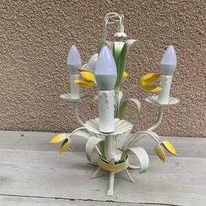K&ouml;nnte beinhalten: Wei&szlig;er Metall-Kronleuchter mit gelben Blumenakzenten und wei&szlig;en Gl&uuml;hbirnen. Der Kronleuchter hat ein florales Design und ist perfekt f&uuml;r ein Bauernhaus oder ein Cottage.