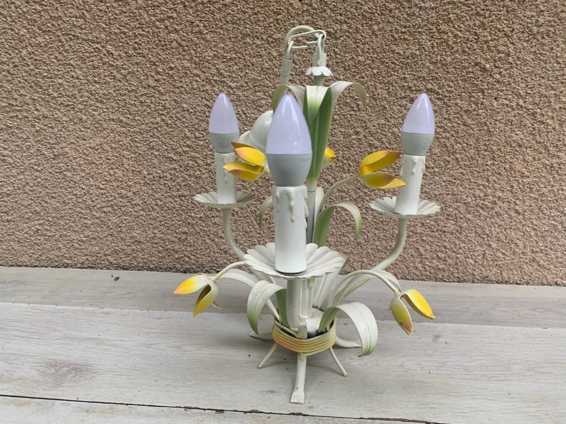 K&ouml;nnte beinhalten: Wei&szlig;er Metall-Kronleuchter mit gelben Blumenakzenten und wei&szlig;en Gl&uuml;hbirnen. Der Kronleuchter hat ein florales Design und ist perfekt f&uuml;r ein Bauernhaus oder ein Cottage.