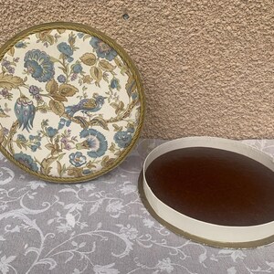 May include: A round, floral patterned box with a gold trim. The lid is open and the inside is lined with a brown fabric.