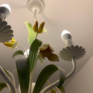 K&ouml;nnte beinhalten: Wei&szlig;e Metall-Luster mit floralem Design. Der Kronleuchter hat f&uuml;nf Lichter und verf&uuml;gt &uuml;ber gelbe und gr&uuml;ne Tulpen.