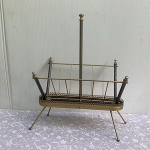 Peut inclure: Un porte-revues en métal doré et noir avec un design décoratif. Le porte-revues a une base rectangulaire et quatre pieds.