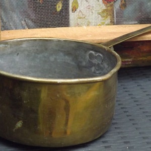 Peut inclure: Une casserole en cuivre vintage avec une patine usée et vieillie. La casserole a un fond arrondi et un bord évasé. La poignée est fixée sur le côté de la casserole.