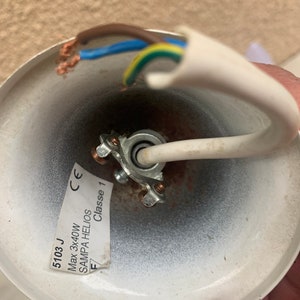 K&ouml;nnte beinhalten: Nahaufnahme einer wei&szlig;en Deckenleuchte mit einem wei&szlig;en Kabel und drei daran angeschlossenen Kabeln. Die Leuchte tr&auml;gt ein Etikett mit der Aufschrift "5103 J Max 3x40W SAMPA HELIOS Classe 1 CE".