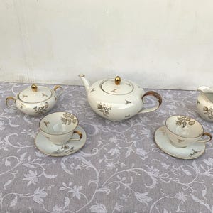 Peut inclure: Un service à thé blanc avec des accents dorés et des motifs floraux. L'ensemble comprend une théière, un pot à crème, un sucrier et deux tasses à thé et soucoupes.