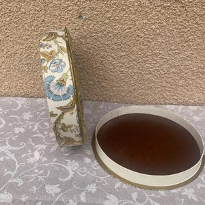 May include: Two round, floral patterned boxes. One box is closed and the other is open, revealing a brown interior.