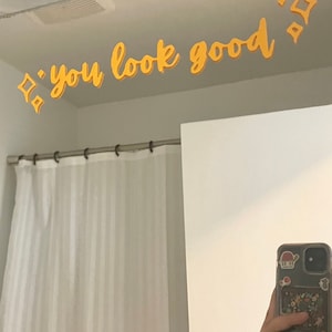 May include: A bathroom mirror with a yellow inscription that reads "you look good" above it. The inscription is decorated with small yellow diamond shapes.