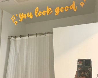 May include: A bathroom mirror with a yellow inscription that reads "you look good" above it. The inscription is decorated with small yellow diamond shapes.
