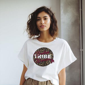 May include: White t-shirt with a round graphic featuring a leopard print design and the text "Badass Tribe Woman".