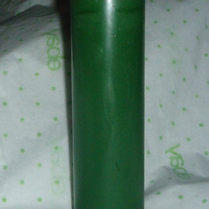 Puede incluir: Una vela de pilar verde oscuro con una mecha blanca.