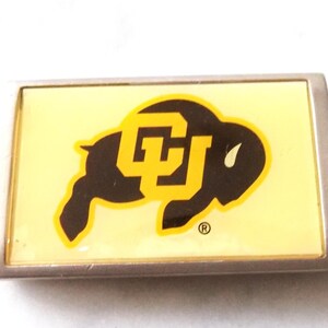 May include: A rectangular keychain featuring the University of Colorado Buffaloes logo. The logo is a black buffalo with a gold "CU" on a yellow background, set in a silver metal frame. The keychain includes a silver key ring.