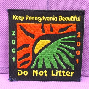 May include: Black and yellow embroidered patch with the text "Keep Pennsylvania Beautiful" and "Do Not Litter". The patch features a stylized sun with green and orange rays.
