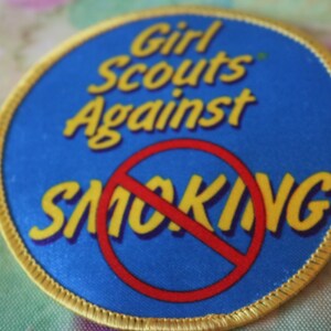 May include: A blue and yellow Girl Scouts Against Smoking patch with a red circle and diagonal line through it.