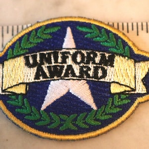 May include: Embroidered patch with the words "UNIFORM AWARD" on a banner, set against a blue background with a white star and green laurel leaves. The patch is approximately 3 inches long.