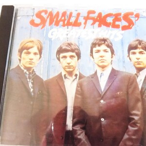 May include: A music CD case featuring the Small Faces' Greatest Hits album cover. The artwork displays four individuals in dark blazers and collared shirts against a blue wooden background. The text reads Small Faces' Greatest Hits in red and white.
