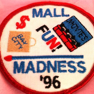 May include: Red, white, and blue embroidered patch with the text "Mall Madness '96". The patch features a shopping bag, a movie ticket, and a matchstick.
