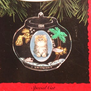 May include: A clear glass Christmas ornament shaped like a fishbowl with a gold fish, a palm tree, and a small cat inside. The ornament has a photo holder in the center. The ornament is labeled "Special Cat Photo Holder".