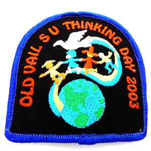 May include: Embroidered patch with a black background and a blue border. The patch features a globe, figures holding hands, a dove, and the text "OLD VAIL SU THINKING DAY 2003" in orange and white.