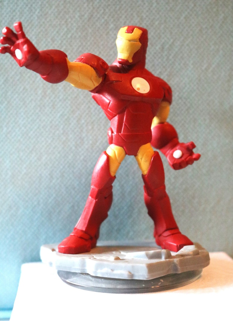 May include: A red and yellow Iron Man action figure stands on a gray base. The figure is posed with one arm outstretched and the other hand clenched into a fist.